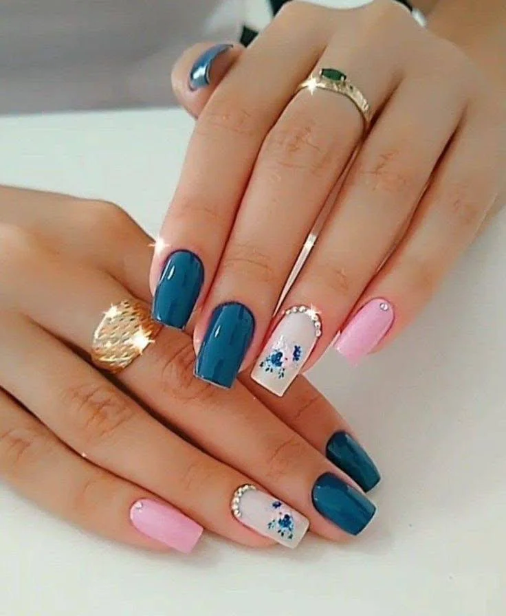 Short nails featuring deep teal, pink, and white with blue floral accent nails, for a glamorous spring-inspired look.