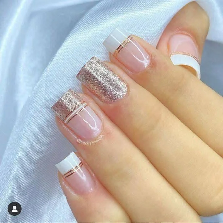 Short nails with a modern French manicure featuring gold stripes and a glitter accent nail, creating a glamorous, updated look.