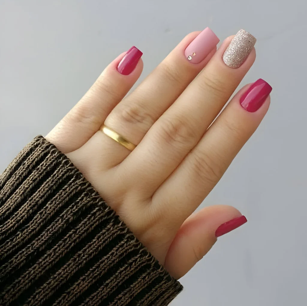 Short nails with magenta, light pink, and pink glitter polish, with small rhinestone accents.