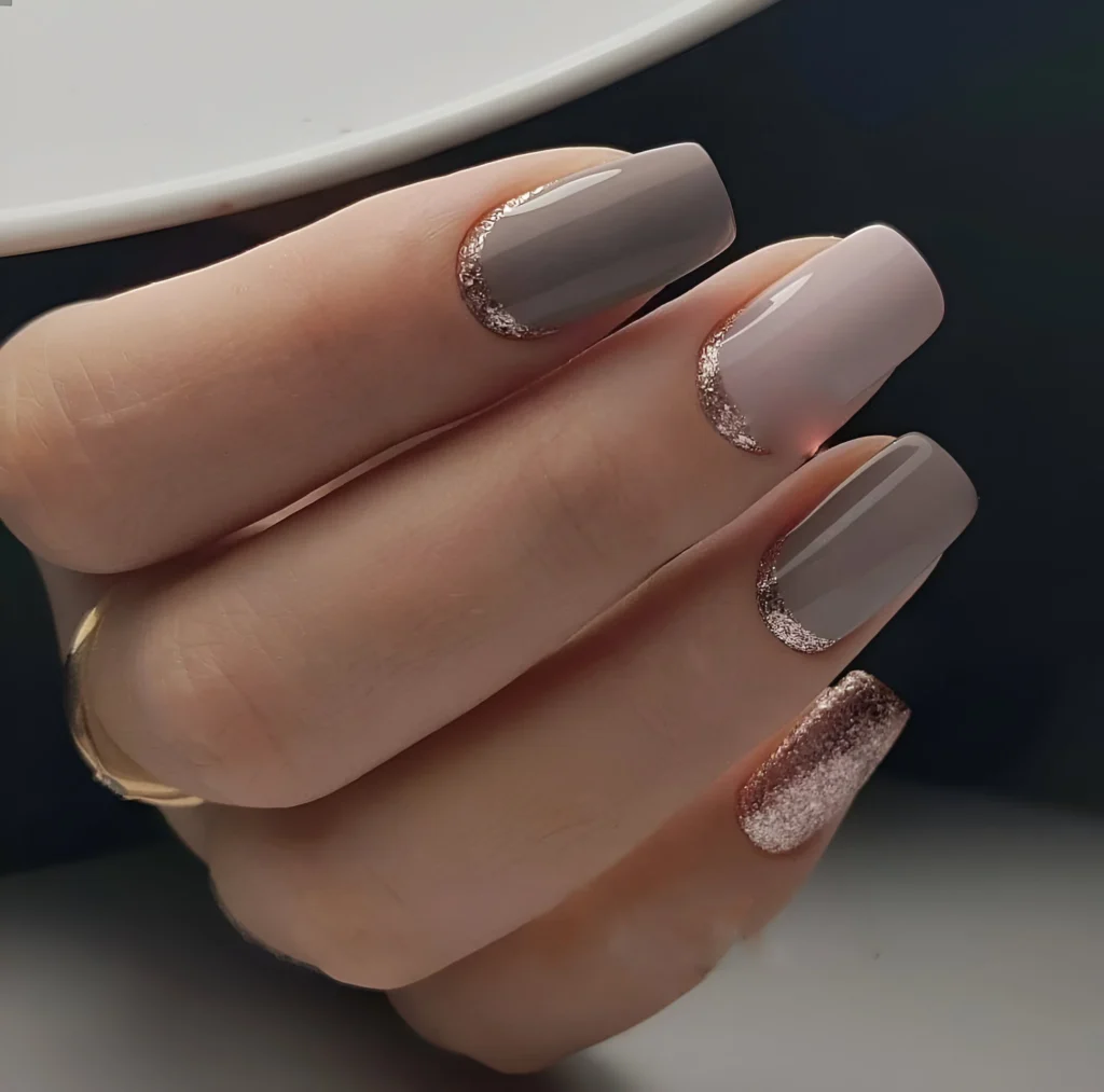 Short nails with light beige and taupe polish, featuring rose gold glitter accents and half-moon designs.