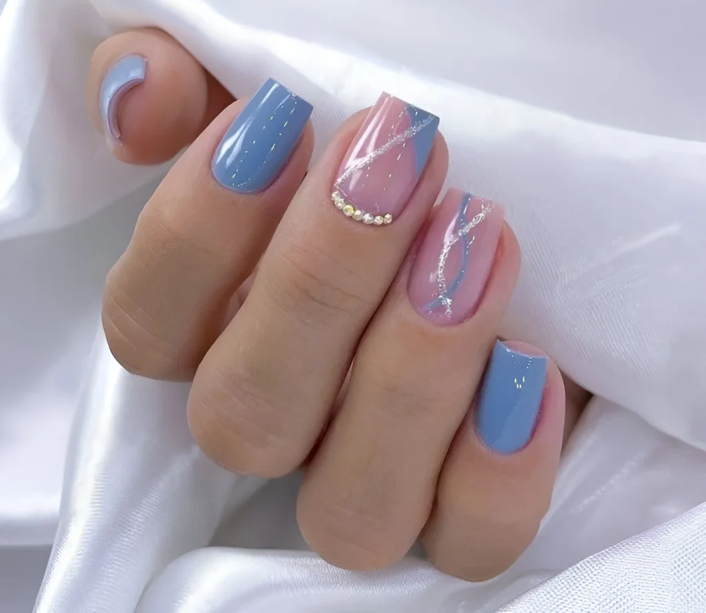 Short nails with pastel blue and pink polish, featuring abstract silver lines and rhinestone accents.