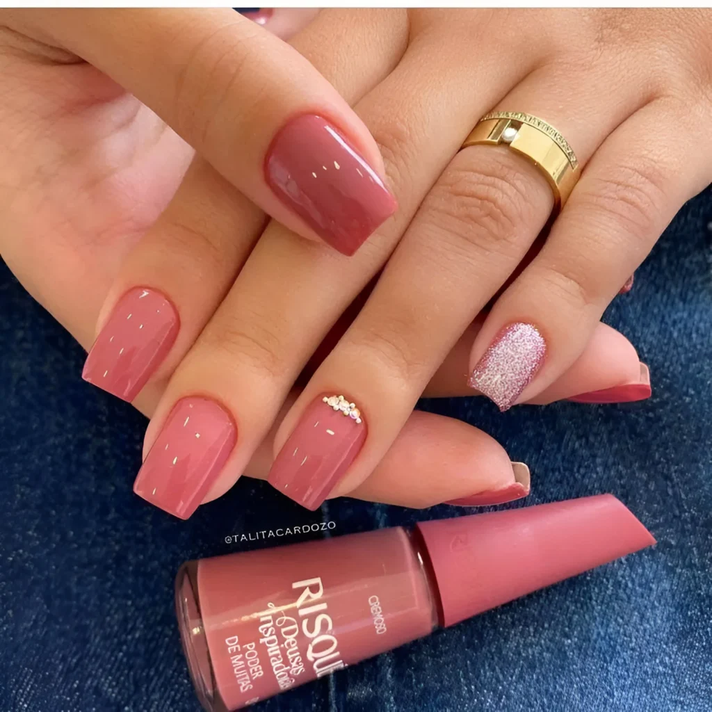 Short nails with a rose-clay toned polish, a rhinestone arc accent, and a pink glitter accent nail.