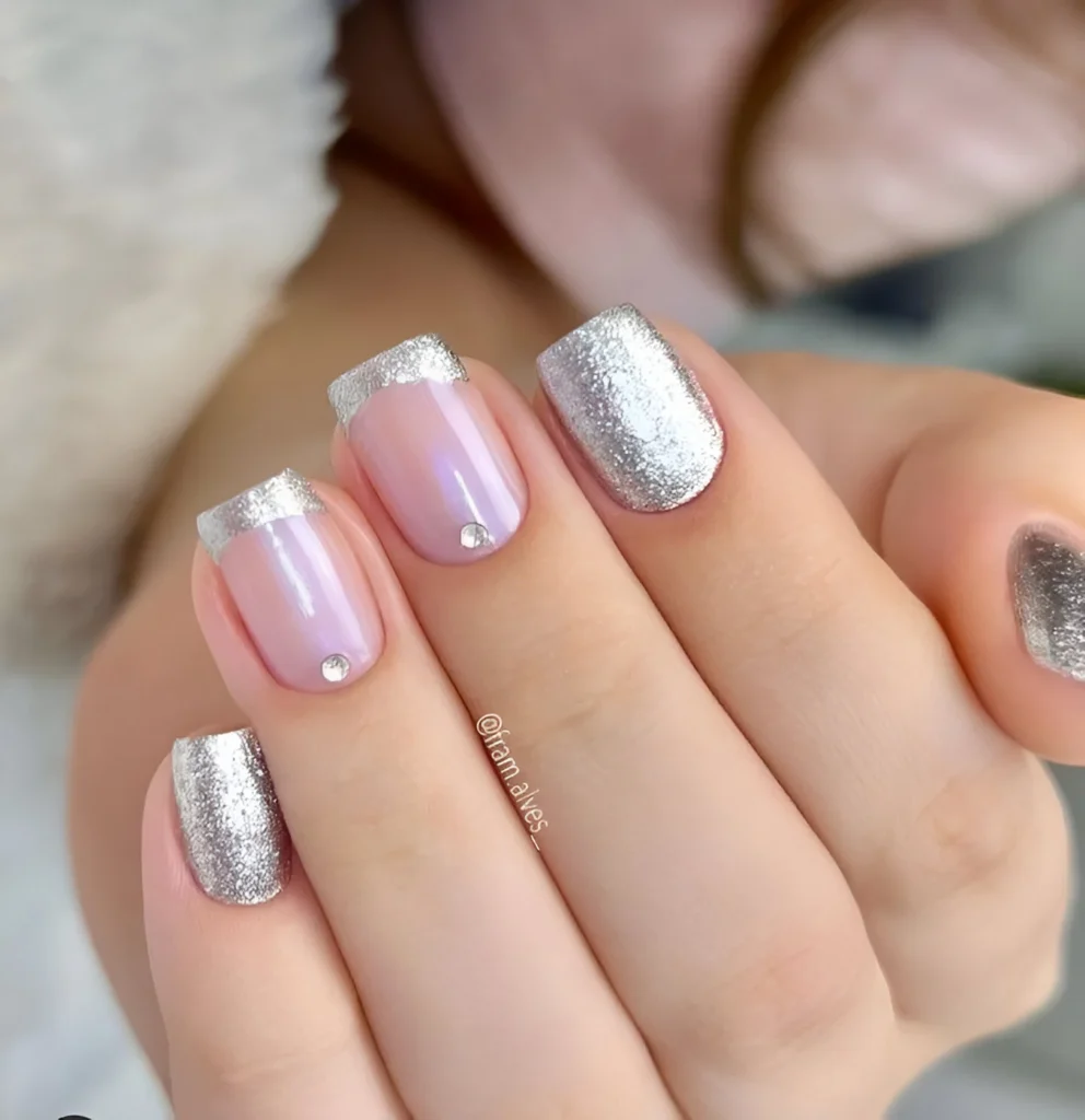 Short nails with a sheer, iridescent base, chunky silver glitter French tips, and rhinestone accents.