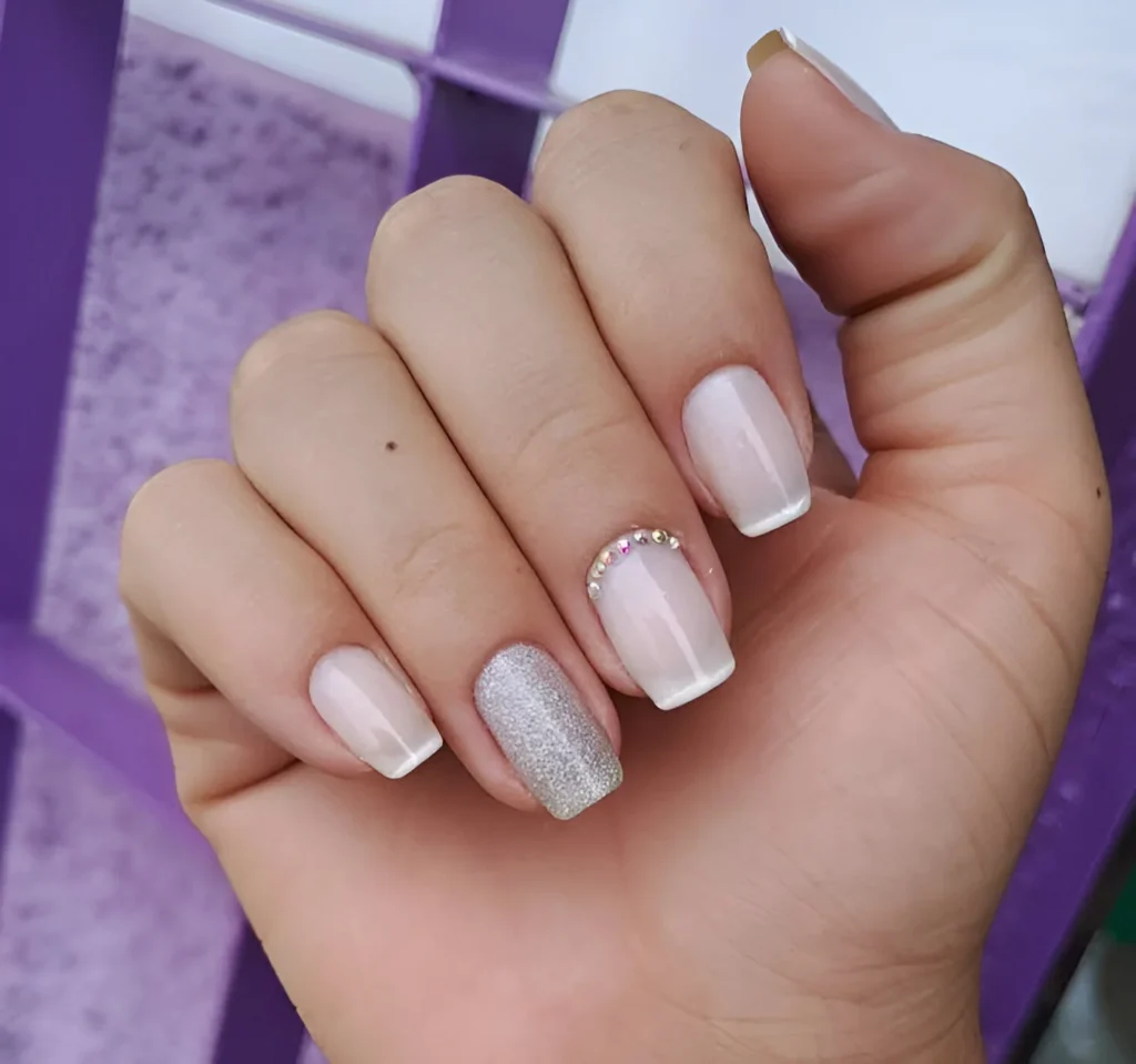 Short nails with white French tips, rhinestone accents, and a silver glitter accent nail.