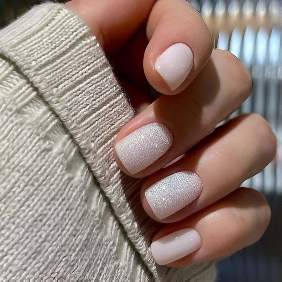 Short white nails with two accent nails featuring fine white glitter.