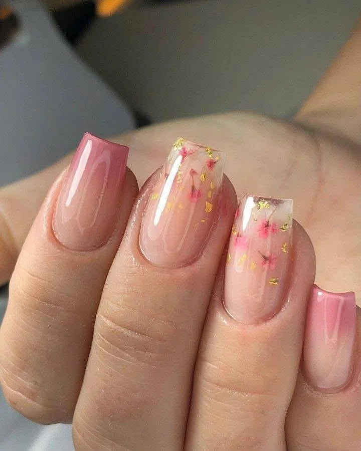 Elegant nail design with encapsulated flowers and gold flakes, with pink ombre.