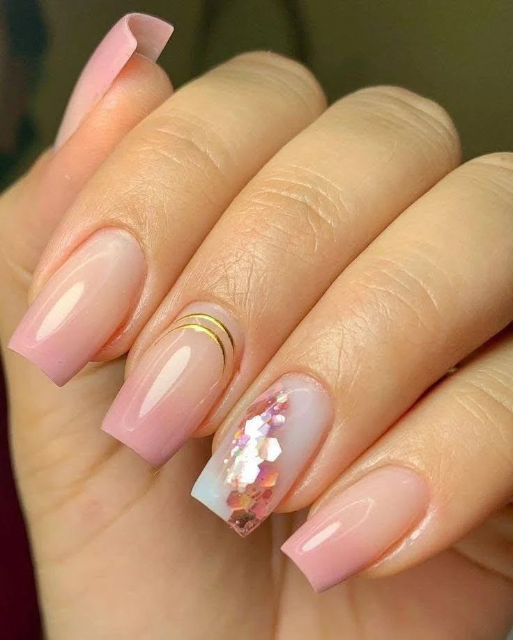 Pink ombre nails with a gold stripe accent nail and glitter.