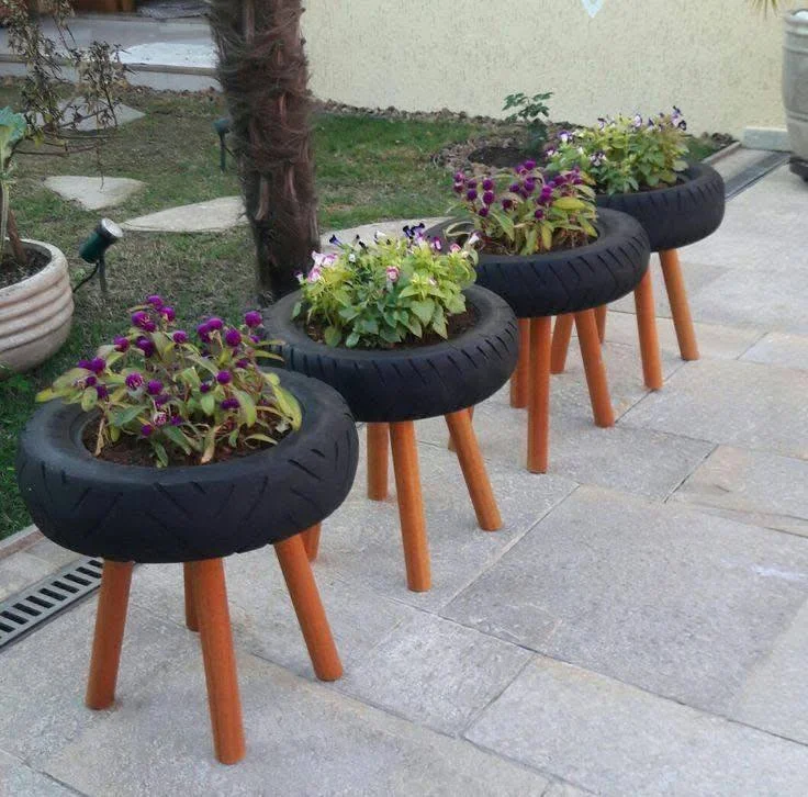 Four upcycled tire planters on wooden legs, with purple flowers.