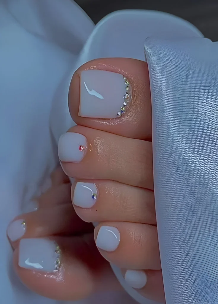 Milky white toe nail design with tiny crystal accents, bridal pedicure.