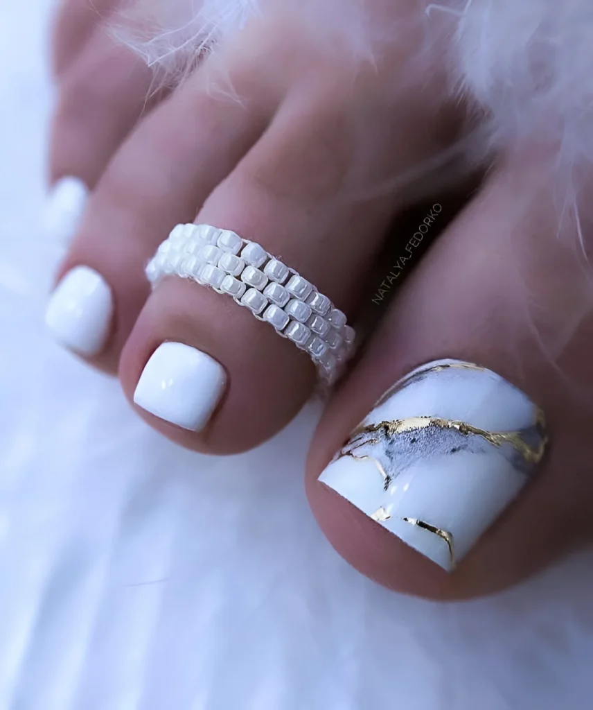 White marble toe nail design with gold foil accents, modern and chic pedicure.