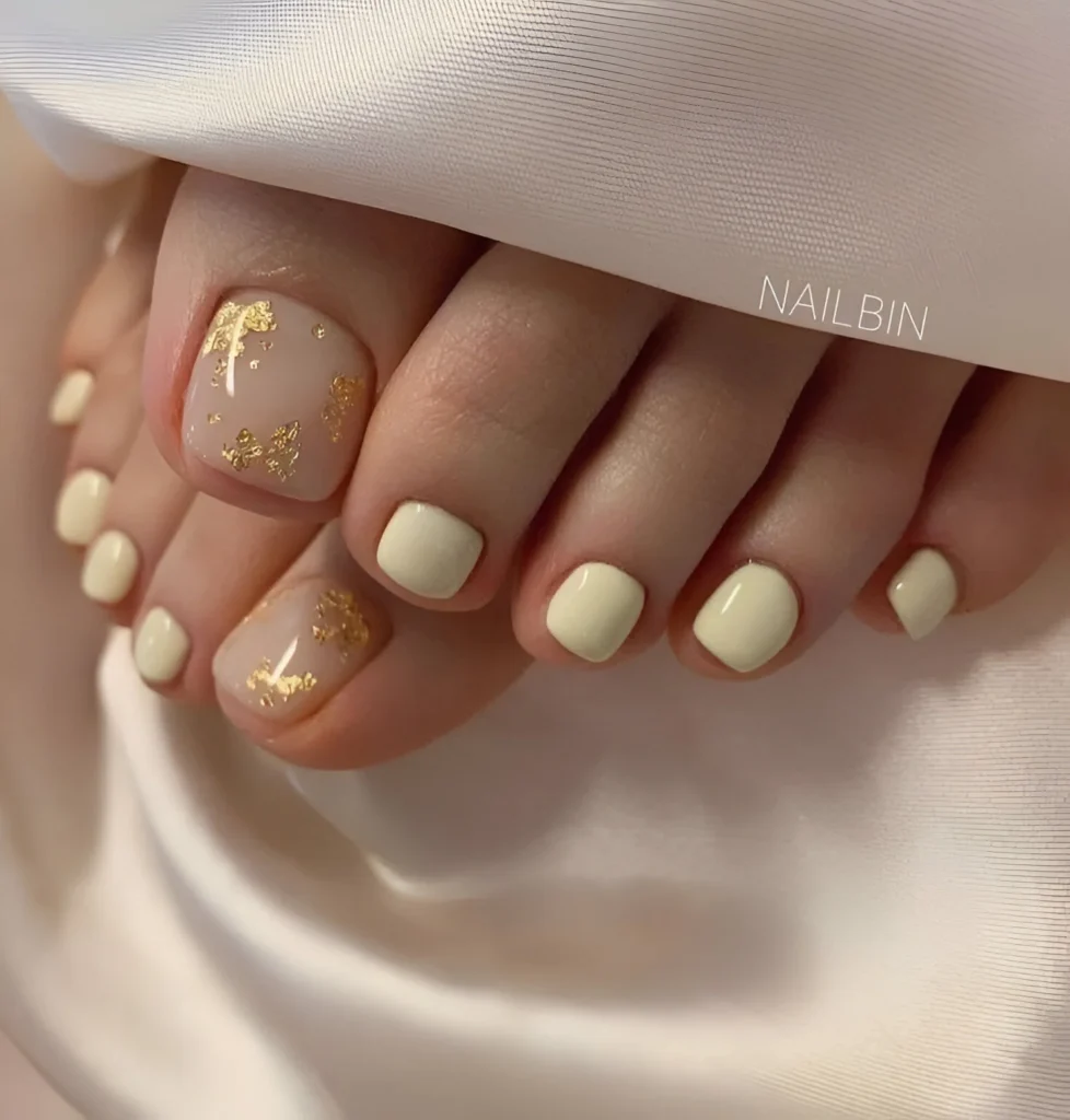 Pale yellow toe nail design with gold foil accents, elegant and minimalist pedicure.