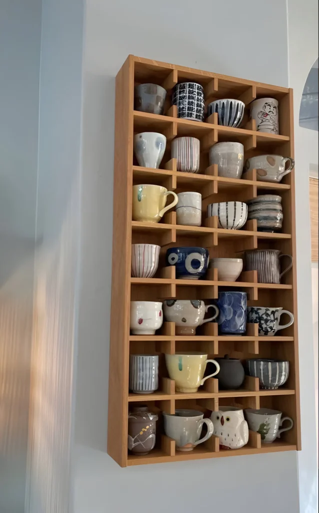 Wall-mounted wooden cubby shelf displaying a collection of mugs.