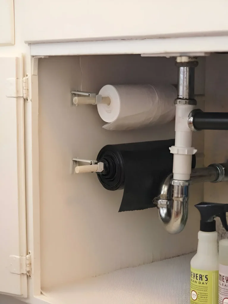 Under-sink cabinet with mounted rods dispensing rolls of trash bags.