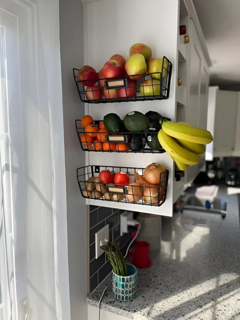 Wall-mounted wire baskets and a shelf storing fruits, vegetables, and canisters in a kitchen.