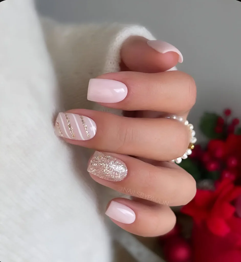 Short, square-shaped nails with a milky pink base. One nail features diagonal stripes of white and silver glitter, while another is fully covered in silver glitter. The remaining nails are solid milky pink.