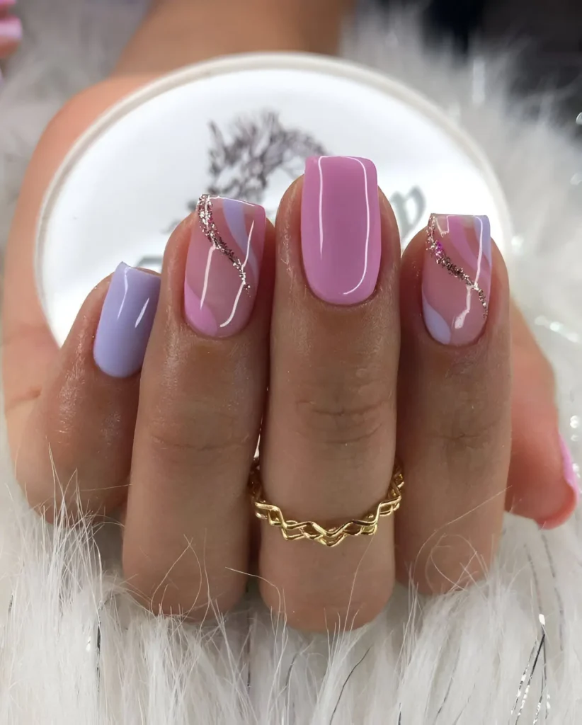 Short, square-shaped nails with a mix of solid pastel pink and lavender, and a marbled design combining both colors with thin, swirling silver glitter accents.