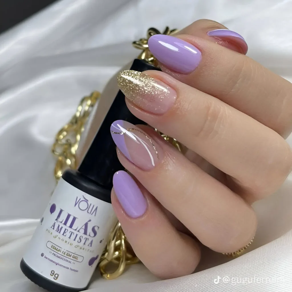 Oval-shaped nails featuring a solid lilac color on most nails, with one accent nail featuring a gold glitter gradient and a thin, abstract white line.