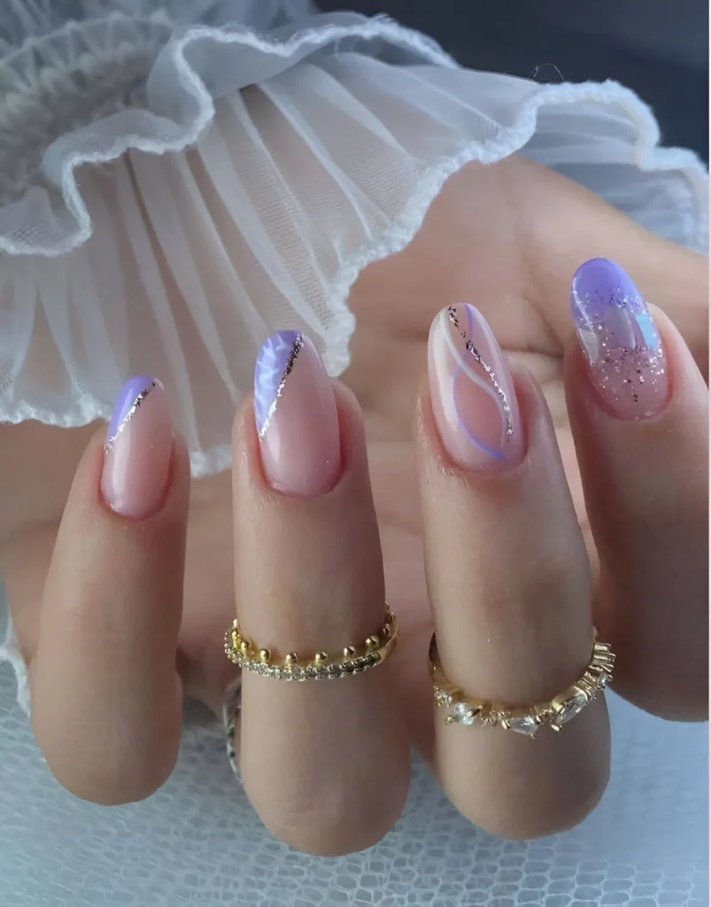 Long, oval-shaped nails with various designs. Some nails feature a lavender-to-clear iridescent gradient, others have a nude base with thin, swirling silver glitter lines, and one has a glitter-tipped French manicure design.