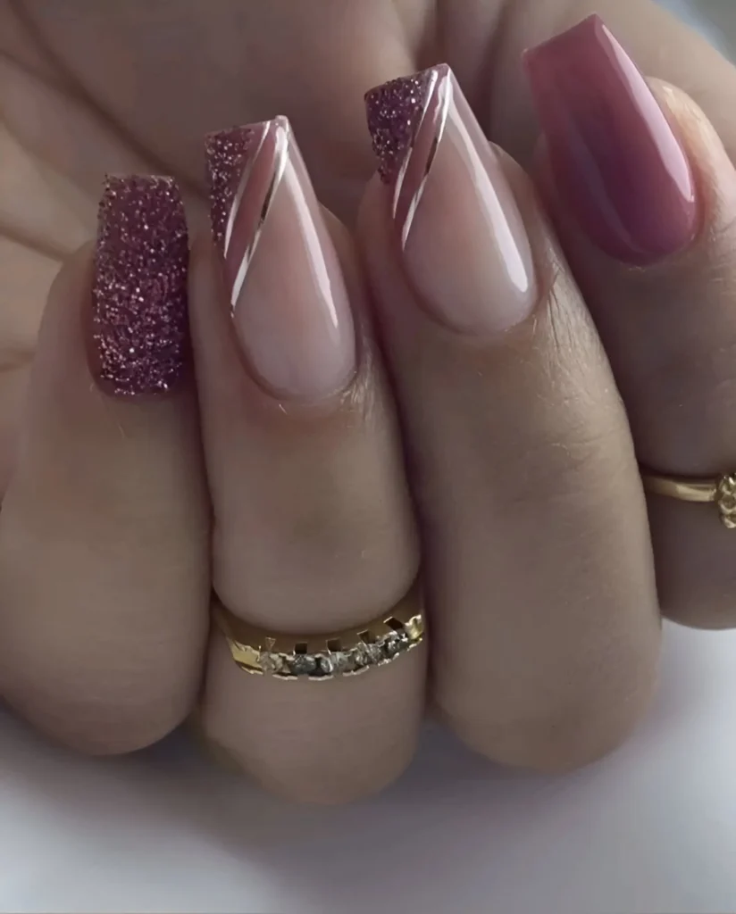 Long, coffin-shaped nails. One nail is solid, glossy deep rose; two have a nude base with a diagonal section of rose-gold glitter separated by a thin white line; one is fully covered in rose-gold glitter.