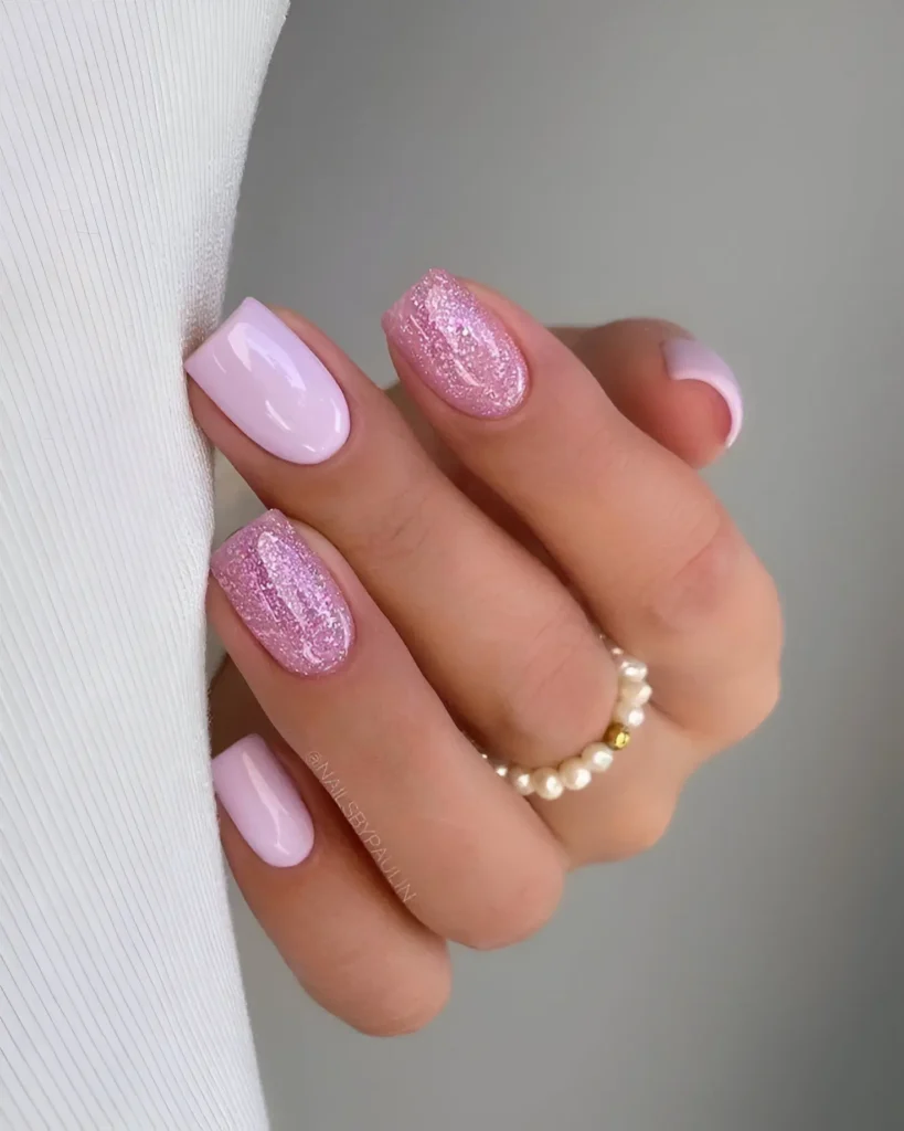 Short, oval-shaped nails. Two nails are painted a solid, light pink, and two are covered in a matching pink glitter.