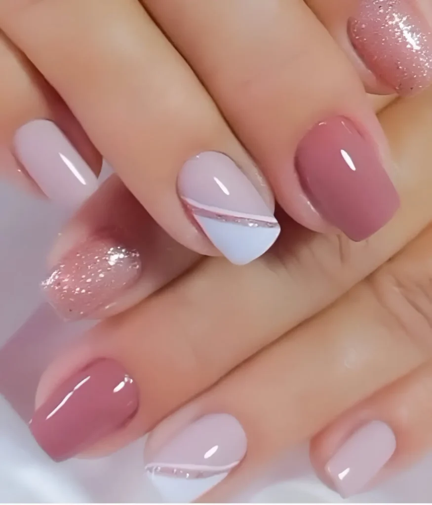 Short, square-shaped nails. Some nails are solid glossy rose in varying shades. Others feature a nude base with a diagonal section of white at the tip, separated by a thin, silver glitter line, resembling a modified French manicure.