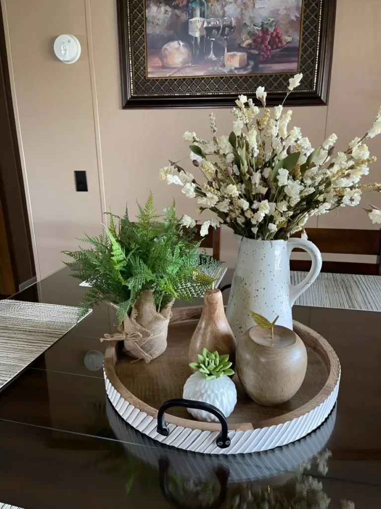 Rustic dining table centerpiece with wood decor, greenery, and ceramic accents in a neutral setting.