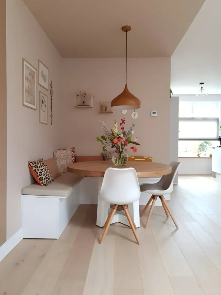 Cozy banquette dining area with a round wooden table, pendant lighting, and decorative accents.