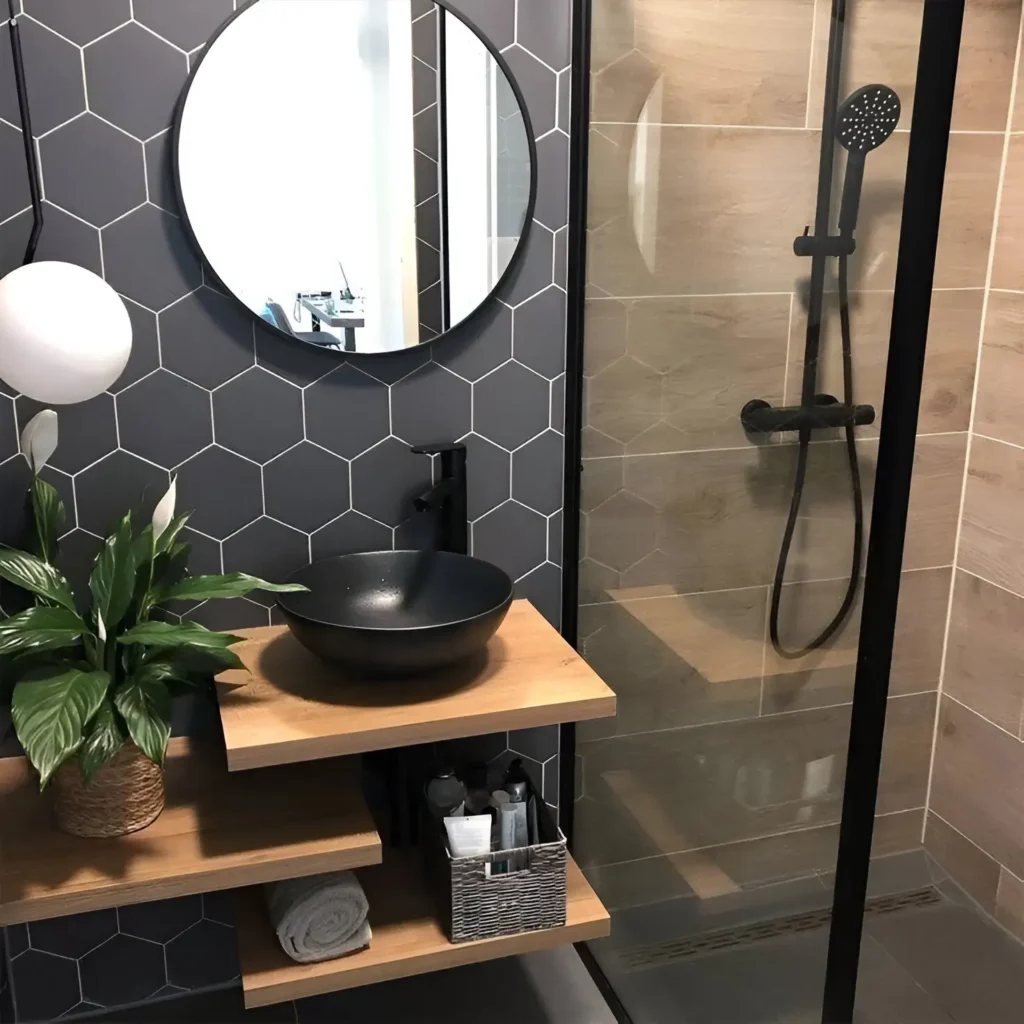 Modern small bathroom with dark hexagonal wall tiles, round mirror, black vessel sink, and wooden floating shelves.