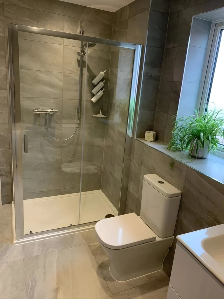 Modern small bathroom with gray tiles, sliding glass shower door, and simple white fixtures.