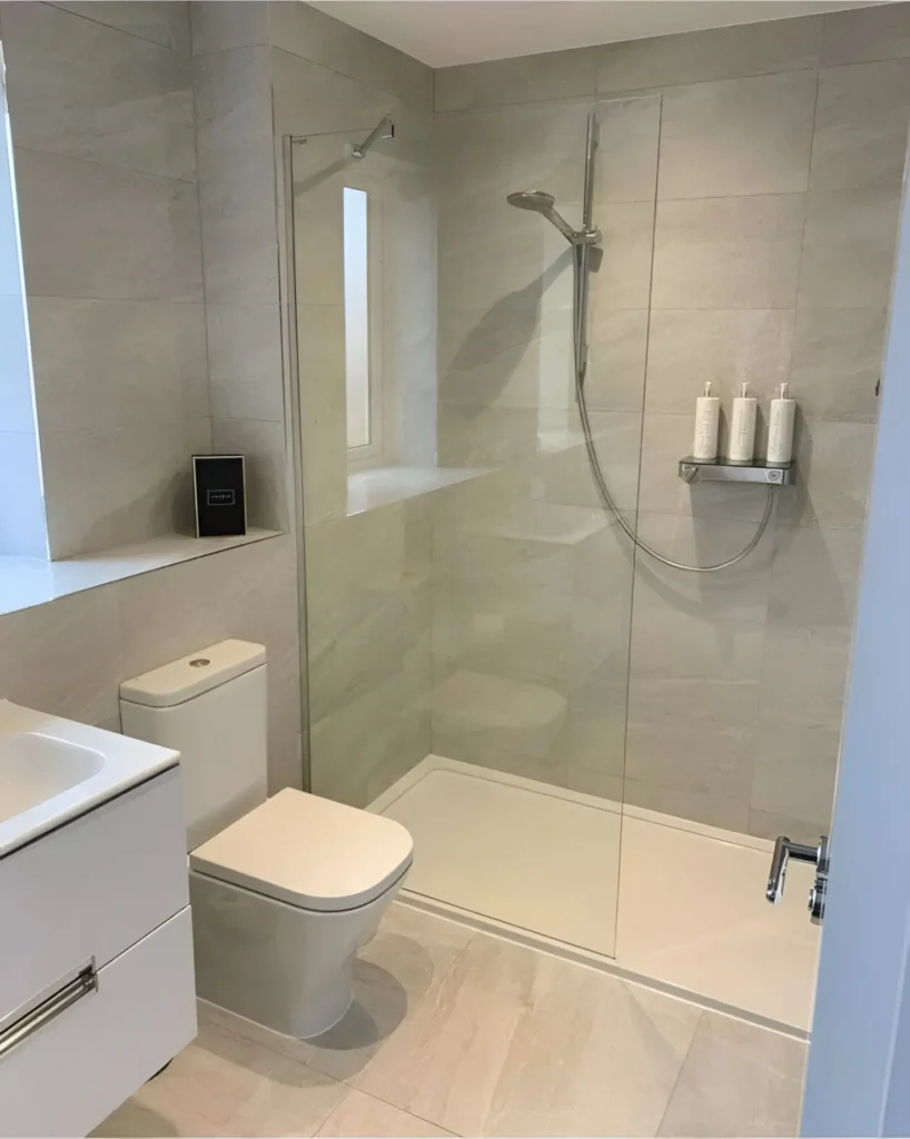 Modern small bathroom with walk-in shower, light gray tiles, and white fixtures.