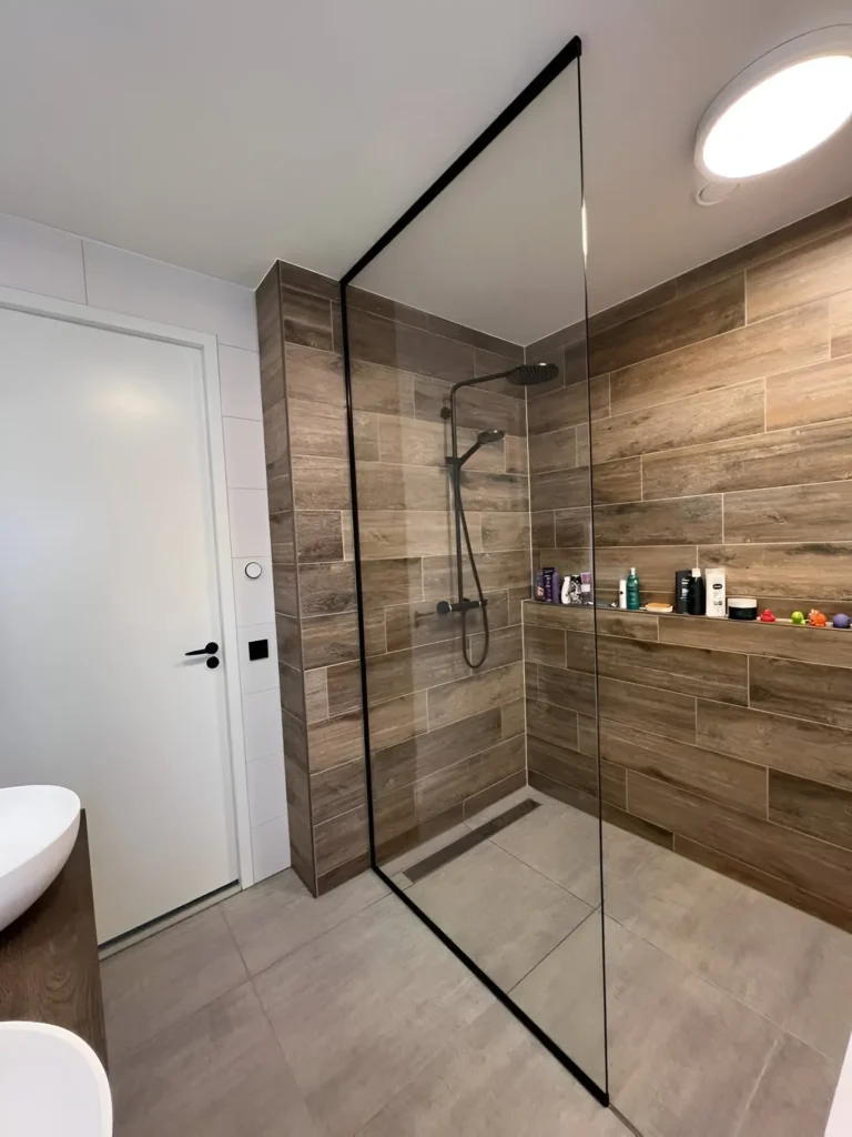 Modern small bathroom with wood-look tile shower, black framed glass panel, and light gray floor tiles.