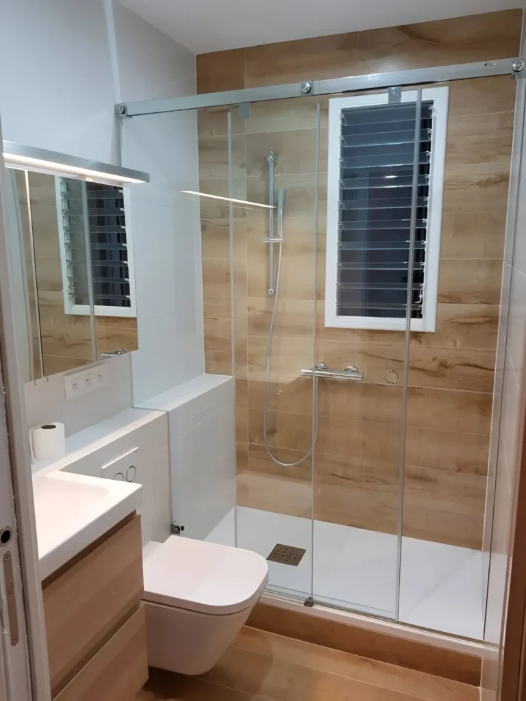 Modern small bathroom with sliding glass shower door, wood-look shower tiles, and a wall-mounted toilet.