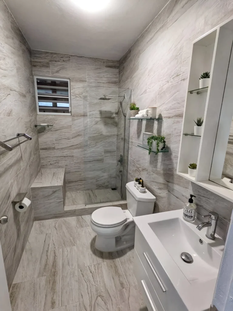 Modern small bathroom with built-in shower bench, light gray and marble-look tiles, and a white vanity.