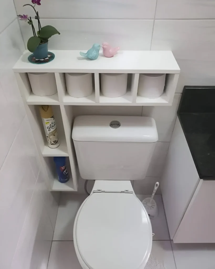 White over-the-toilet storage cabinet with open cubbies, holding toilet paper, air freshener, and small decorative items.