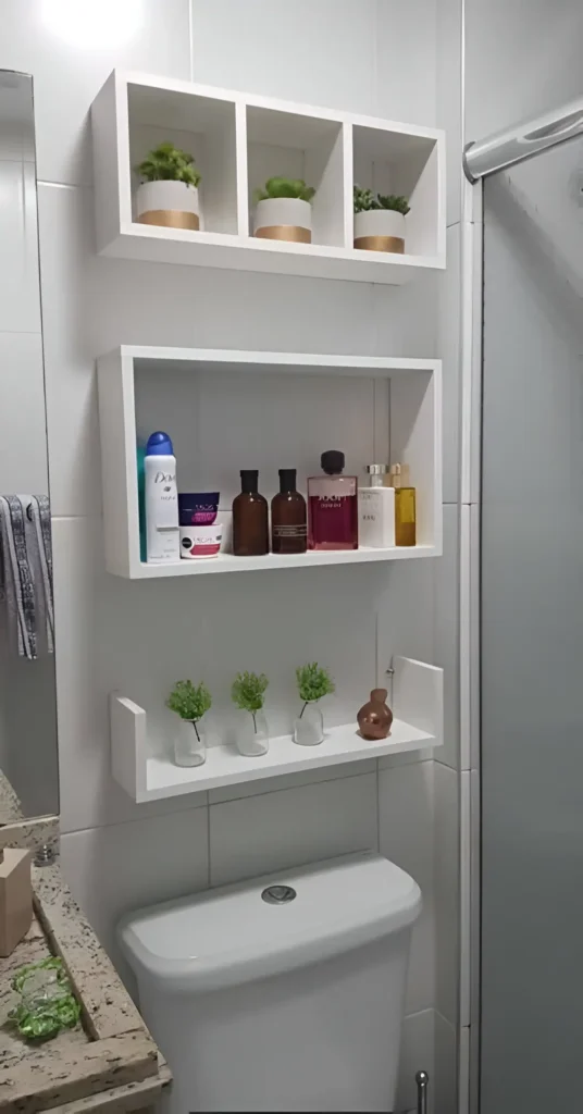 Three white floating shelves mounted above a toilet; the top shelves are square, the middle is rectangular, and the bottom is a U-shape, displaying toiletries and small plants.