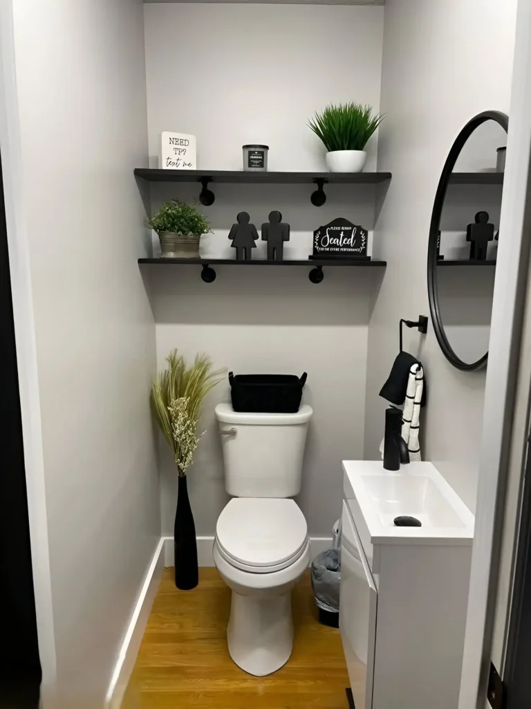 Small bathroom alcove with black shelves installed above the toilet and continuing above a small white sink; shelves decorated with plants, small figurines, and a tissue box.