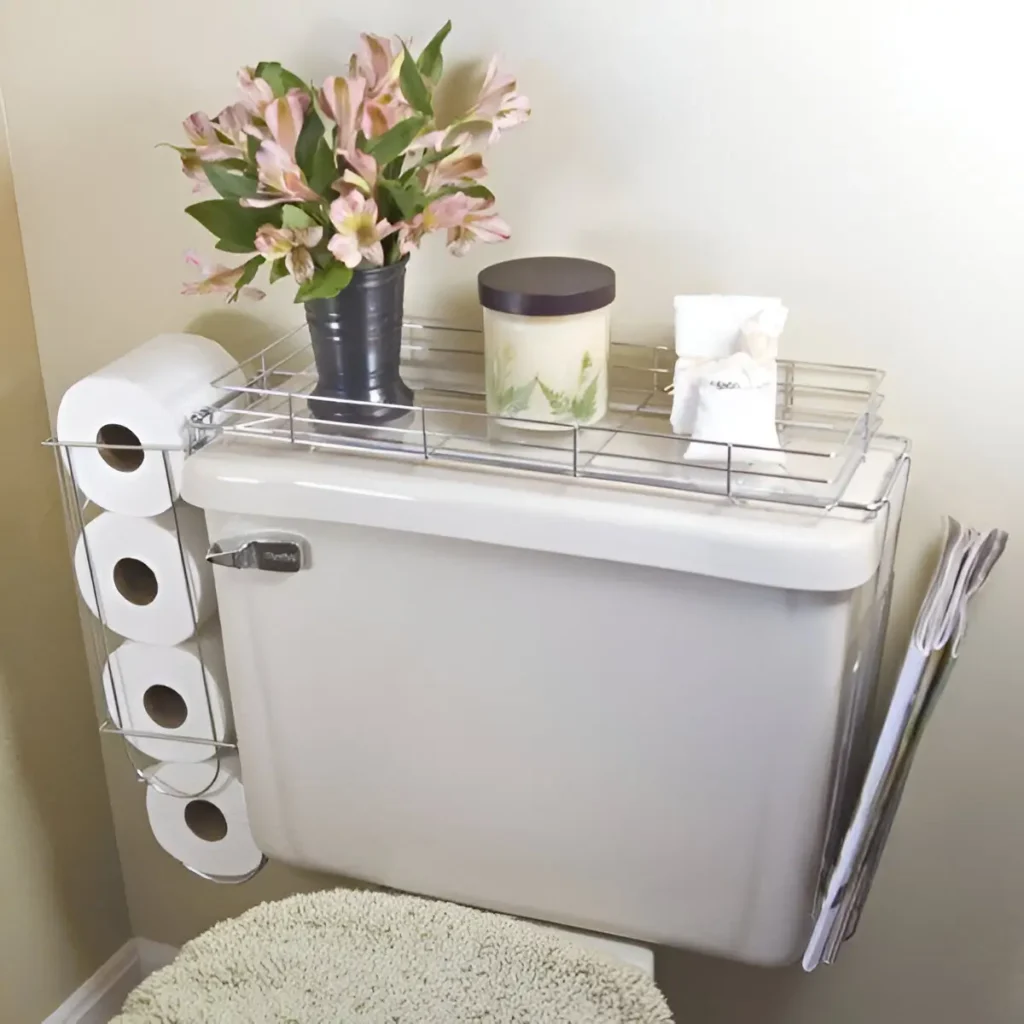 Wire caddy placed on top of a toilet tank, holding toilet paper rolls on one side, a vase of flowers, a candle, and small toiletries on the top shelf, with magazines leaning against the side.