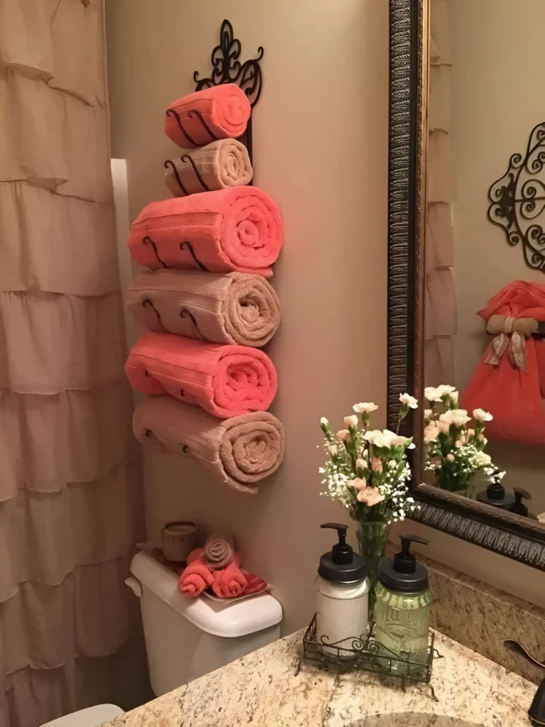 Dark metal vertical towel rack mounted on a wall next to a toilet, holding several rolled towels in alternating coral and beige colors.