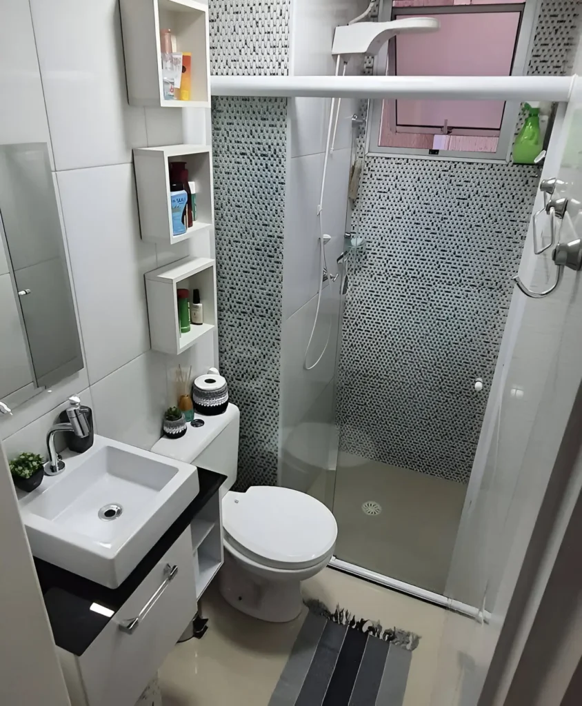 Small bathroom with three white box shelves stacked vertically above the toilet; shelves hold toiletries and small decorative items; a vanity with drawers is next to the toilet.