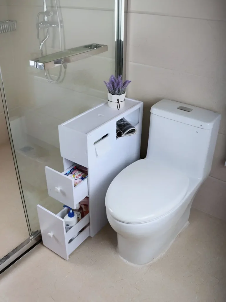 Small white storage unit with three drawers and a built-in toilet paper holder placed next to a toilet; the top of the unit holds a small potted plant. Small Bathroom Storage Ideas