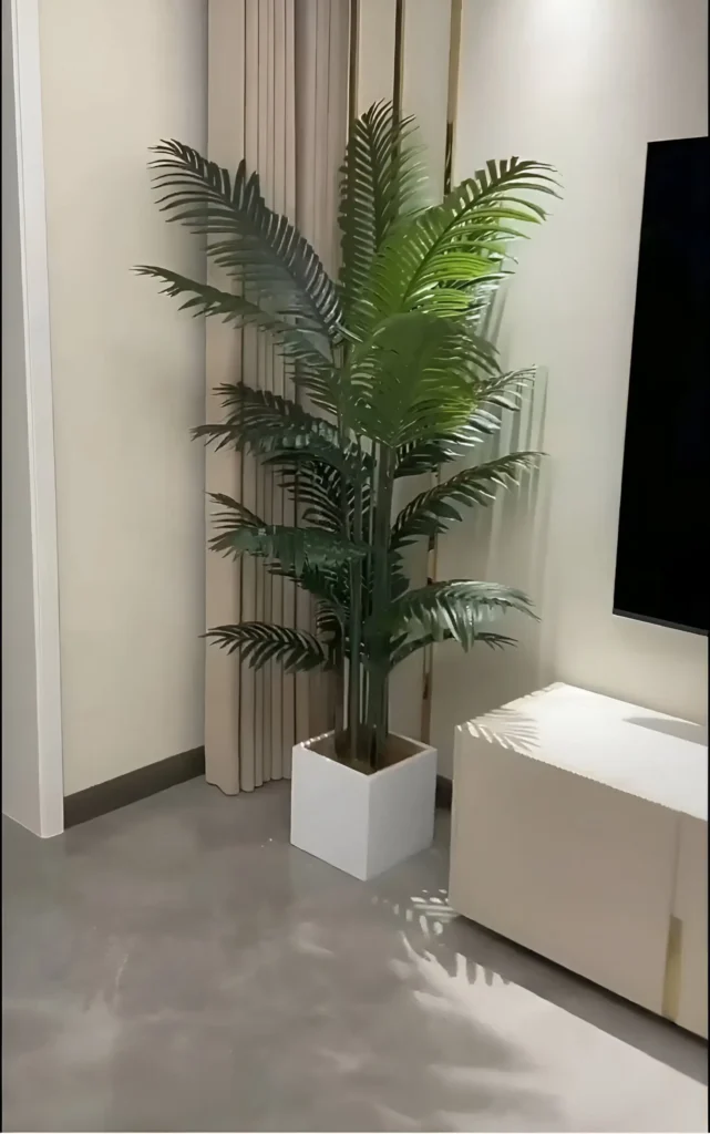 An artificial palm tree in a square, white pot, positioned in a corner of a room, adding greenery without requiring natural light.