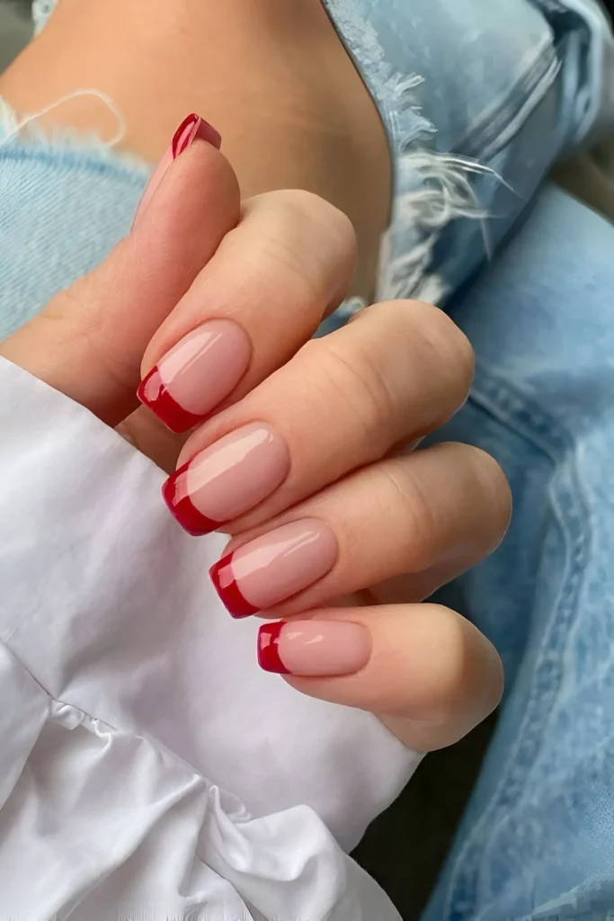 Red French tip nails with a nude base for a modern and chic manicure.