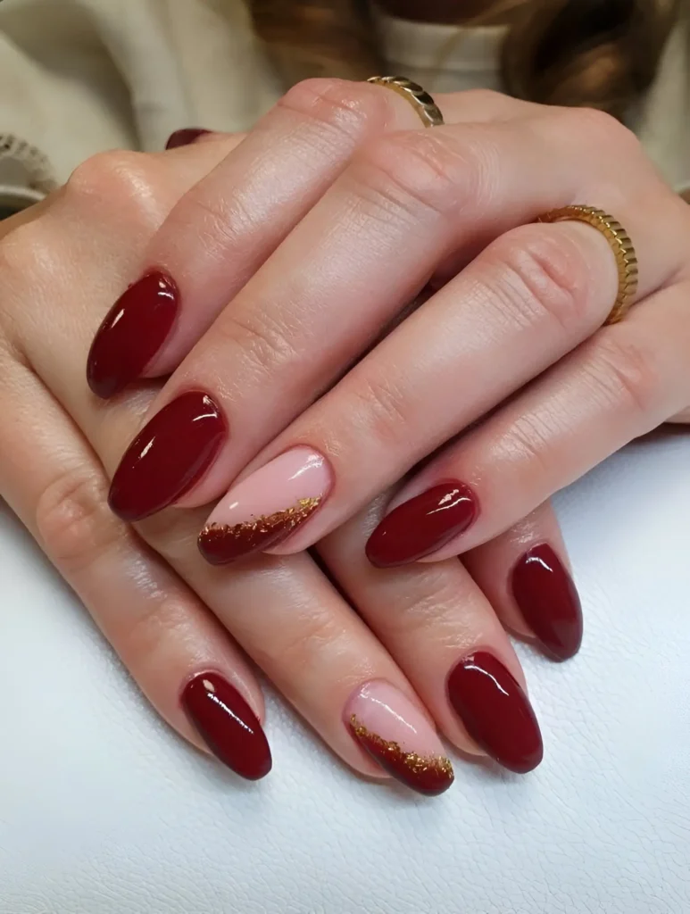 Deep red almond nails with gold glitter accents for a bold and elegant look.