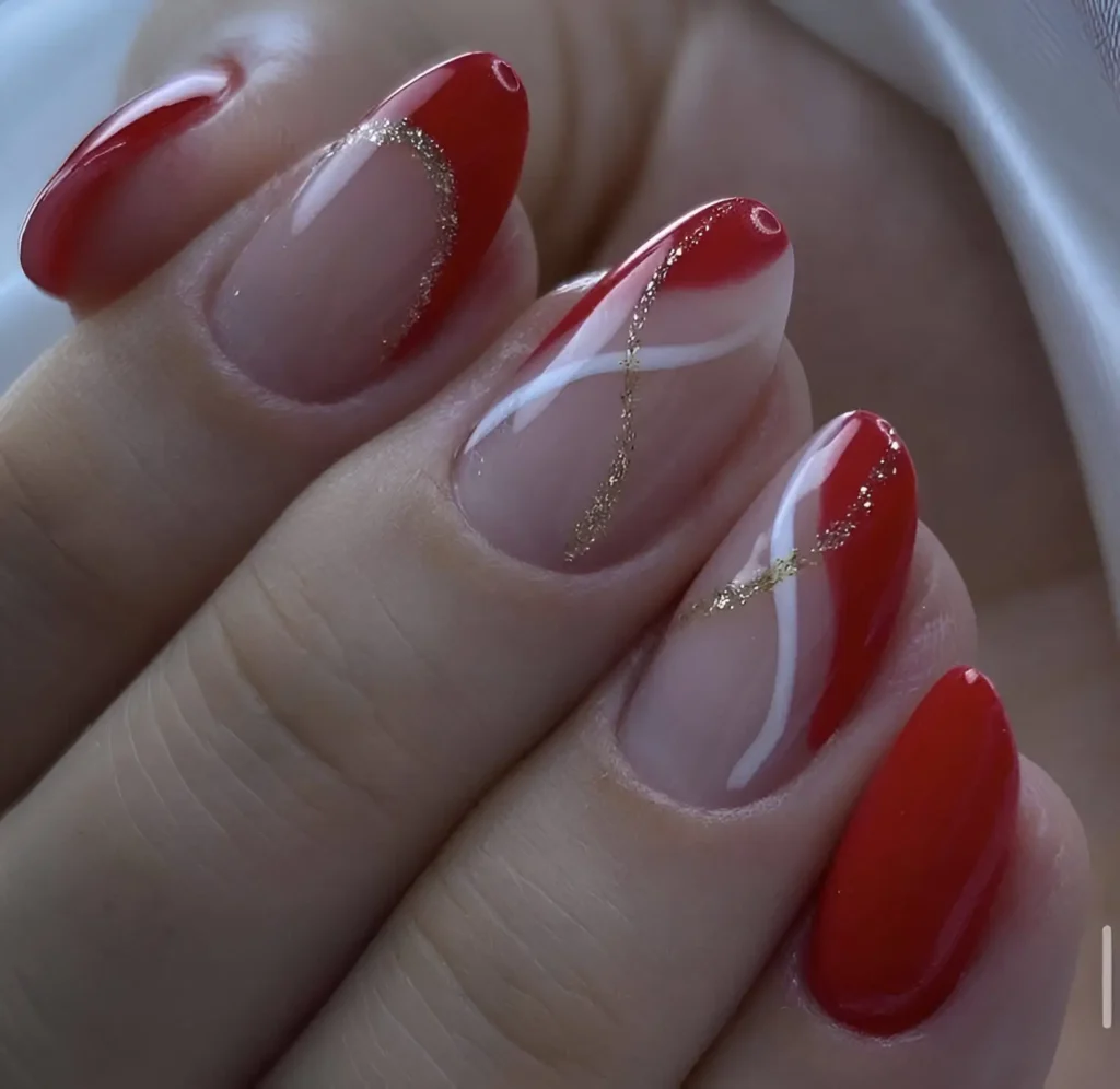 Red and sheer nails with gold and white swirls for an elegant and artistic manicure.