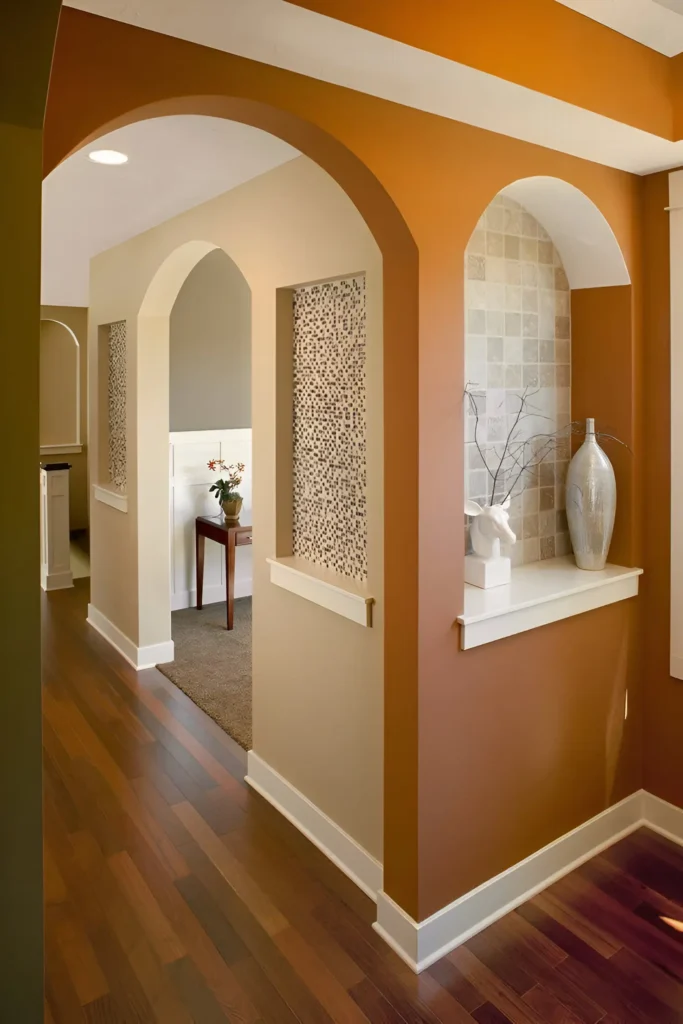 Interior hallway with warm orange painted archways and niches, white trim, hardwood floors, and a view into another room with neutral decor.