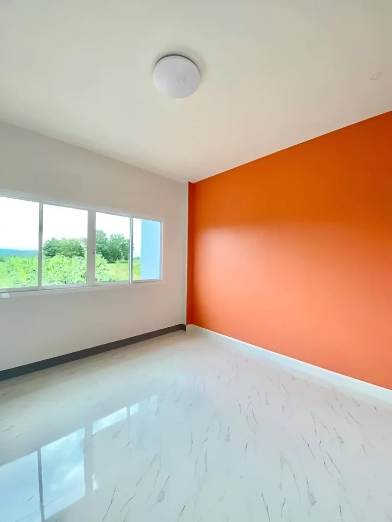 Empty room with a bright orange accent wall, white walls, white tiled floor, and three large windows showing a green landscape.