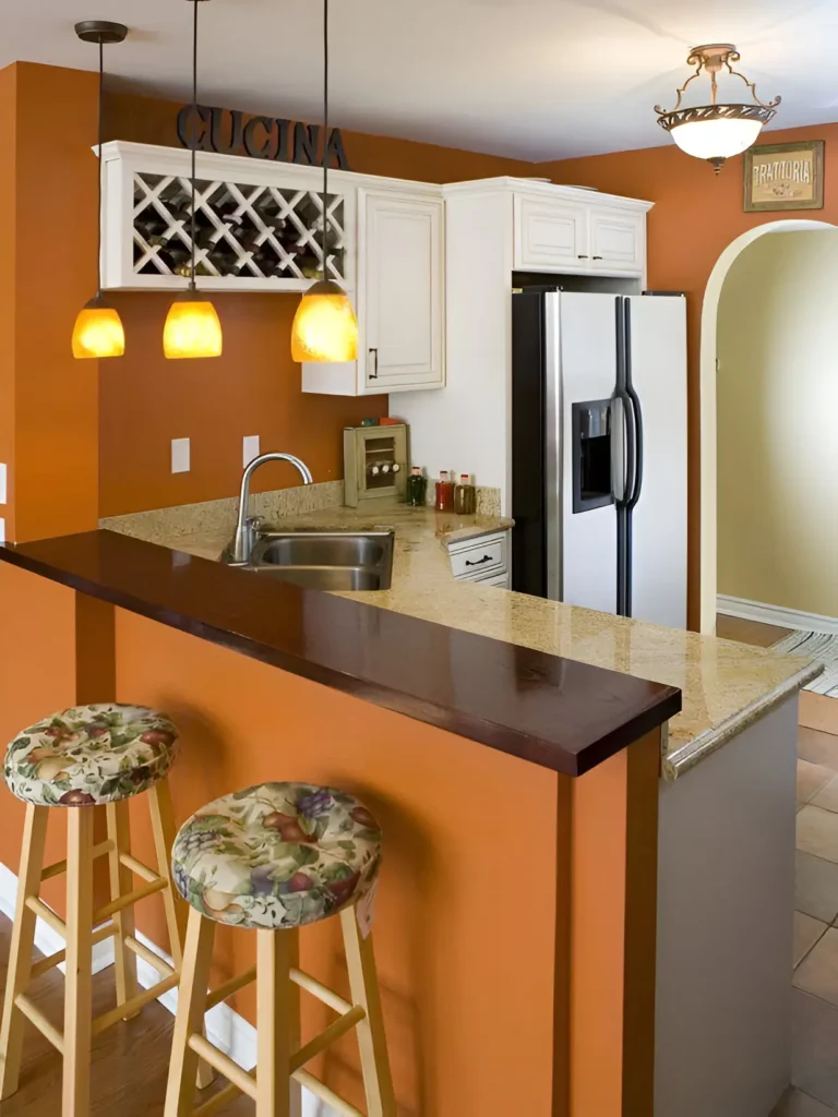 Kitchen/bar area with warm orange walls, white cabinetry, a granite countertop, a dark wood bar top, two bar stools with floral cushions, pendant lights, and a wine rack.