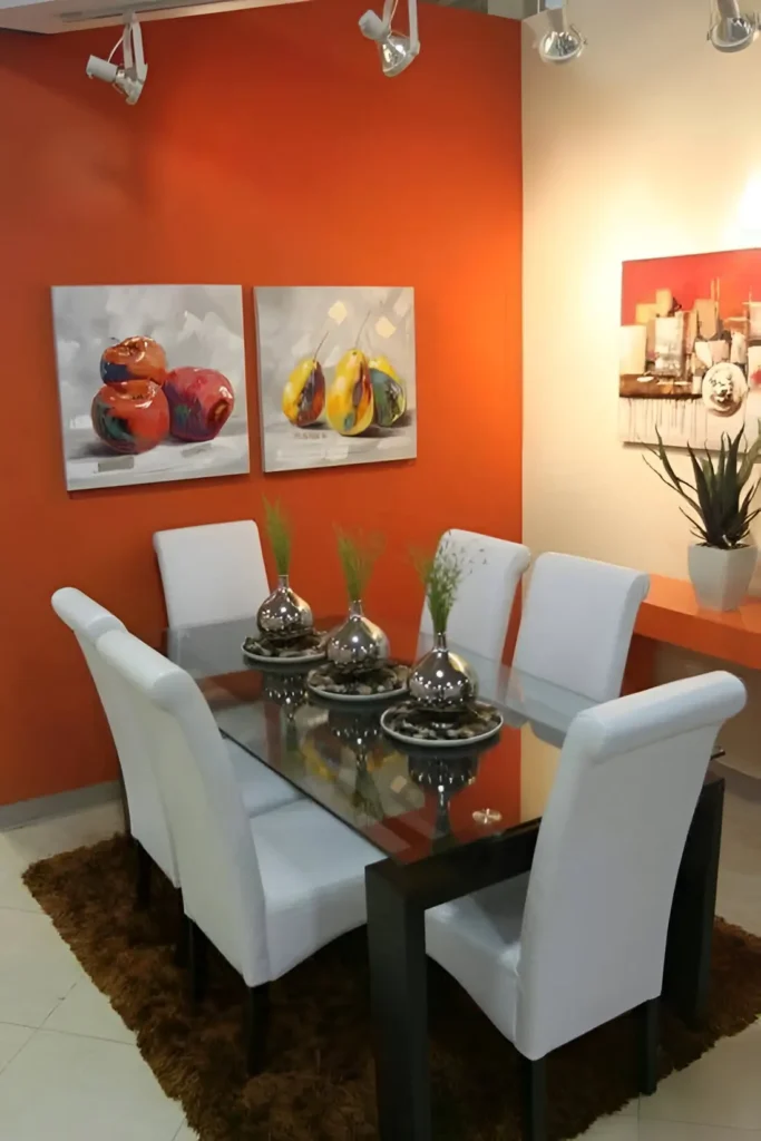 Dining room with an orange accent wall, a dark wood dining table with a glass top, white upholstered dining chairs, a dark brown rug, and two pieces of artwork featuring fruit.  Warm Orange Home Decor