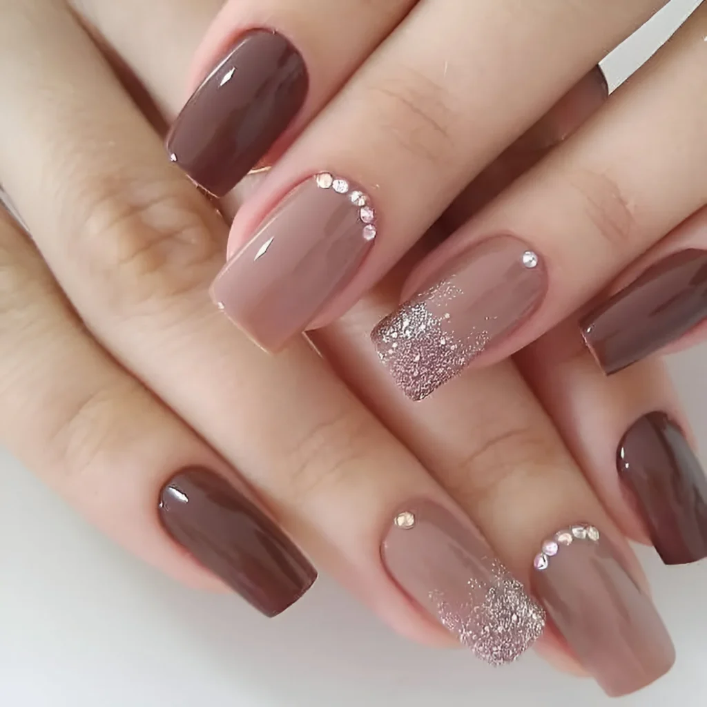 Elegant nail design featuring brown tones, rhinestones, and glitter accents.