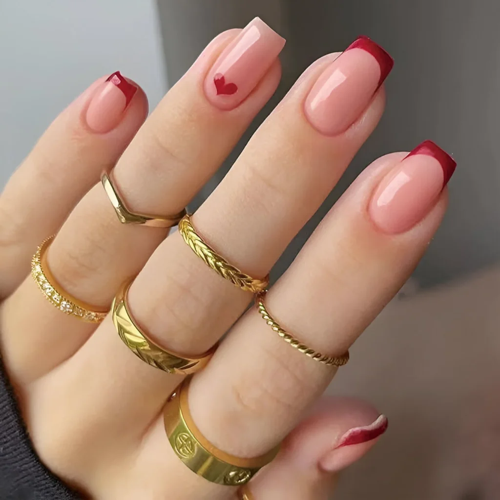 : Elegant French manicure with red tips and a small heart accent.